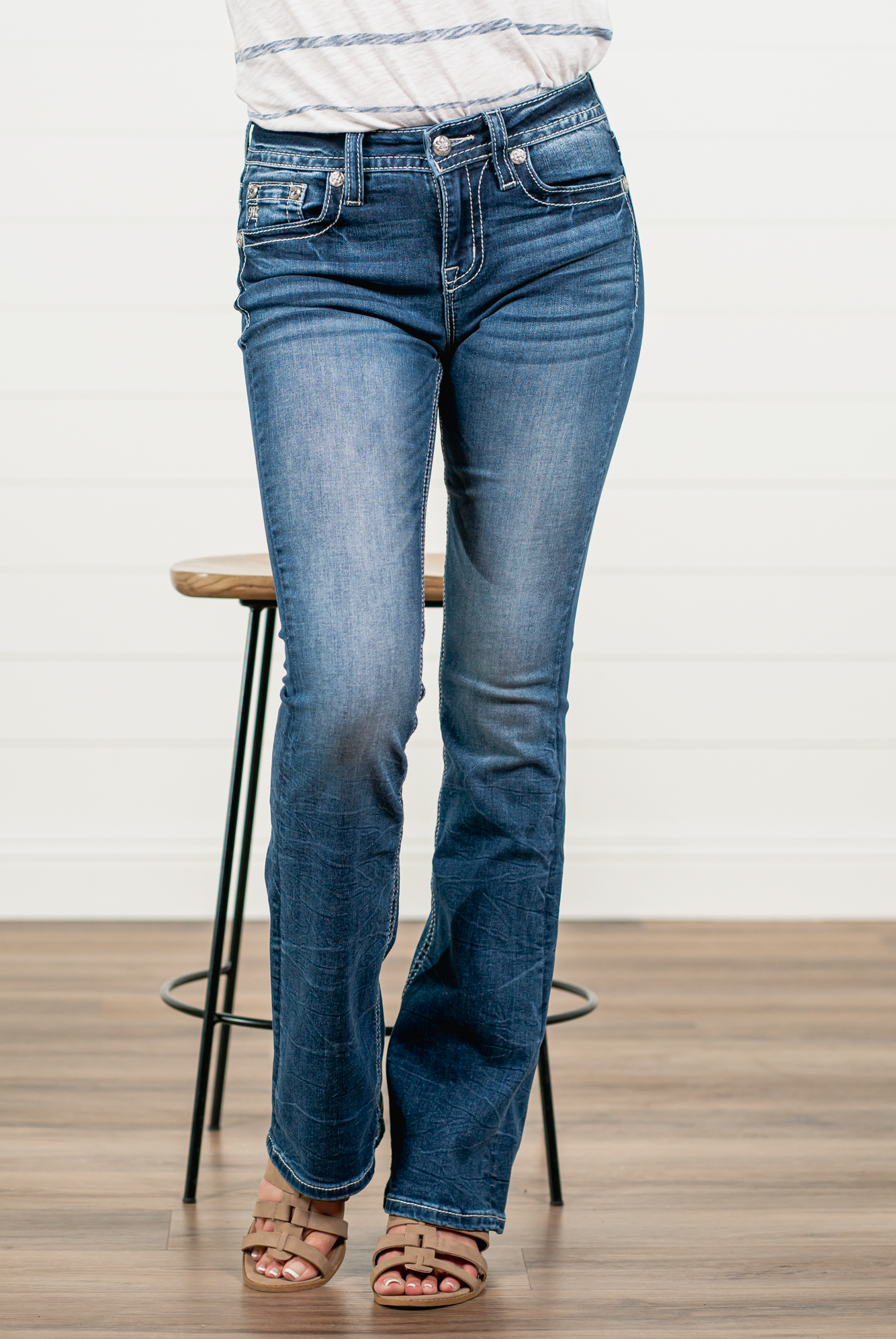 Miss Me Stay sassy and sweet in this bootcut detailed with whiskering, distressing, and embroidered back pocket with rhinestone rivets. Wear these every day to bling up your wardrobe. Wash: Medium Blue Inseam: 34" Boot Cut* Mid Rise, 9" Front Rise* Silver Buttons and Rivets Bright Clear Crystals Fading & Whiskering Details 91% Cotton 6% Polyester 3% Elastane Style #: M3845B Contact us for any additional measurements or sizing. *Measured on the smallest size, measurements may vary by size.